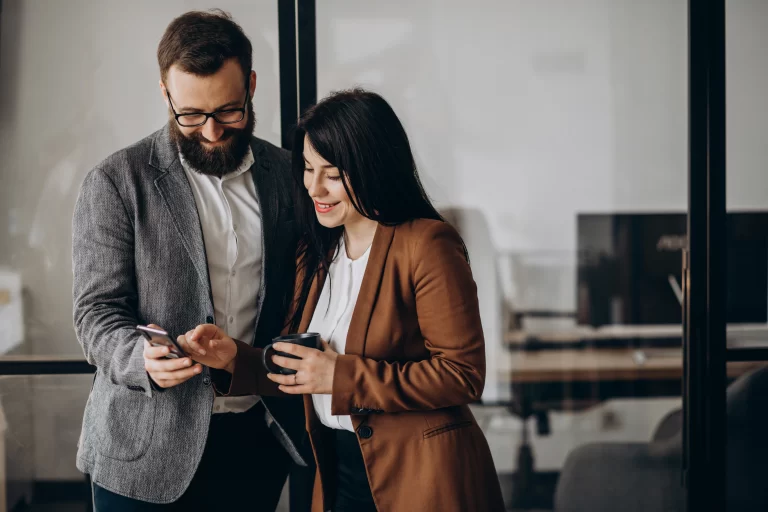 Two business professionals engaged in a discussion while looking at a smartphone, highlighting effective business communication in a modern office setting