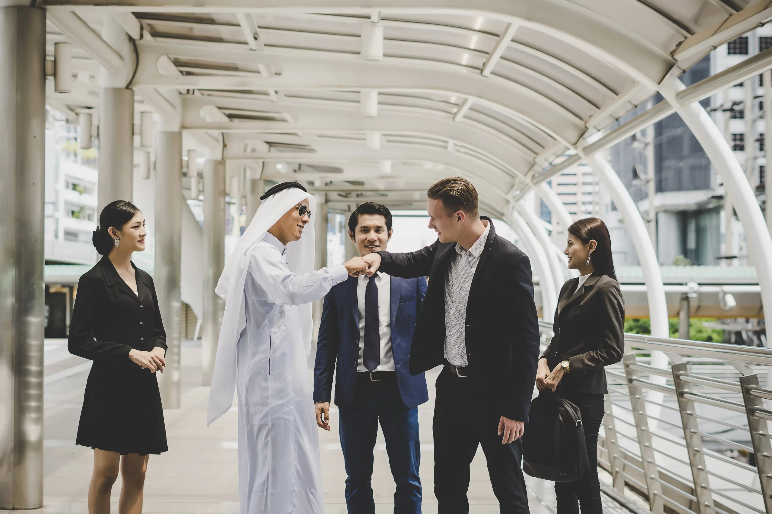 Group of diverse business professionals, including an Emirati man and colleagues, greeting and discussing work in a modern outdoor setting